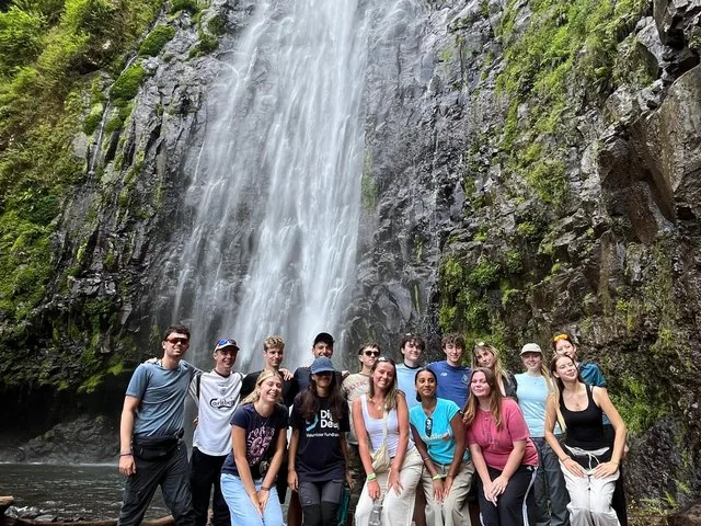 A group of young people posing for a photo in front of a waterfall.