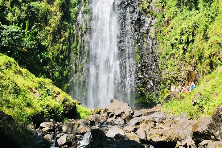 Une grande cascade dévalant les rochers, avec un groupe de personnes assises à proximité.