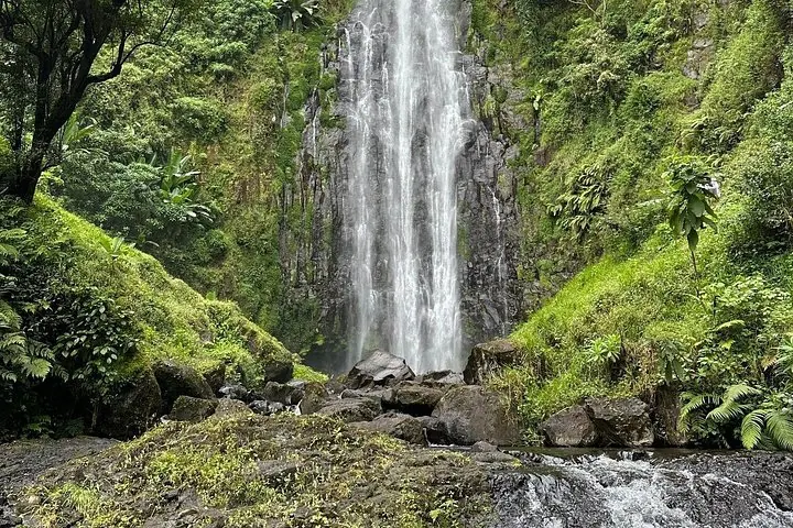 Une belle cascade haute qui s'écoule sur un terrain rocheux entouré d'une végétation luxuriante.